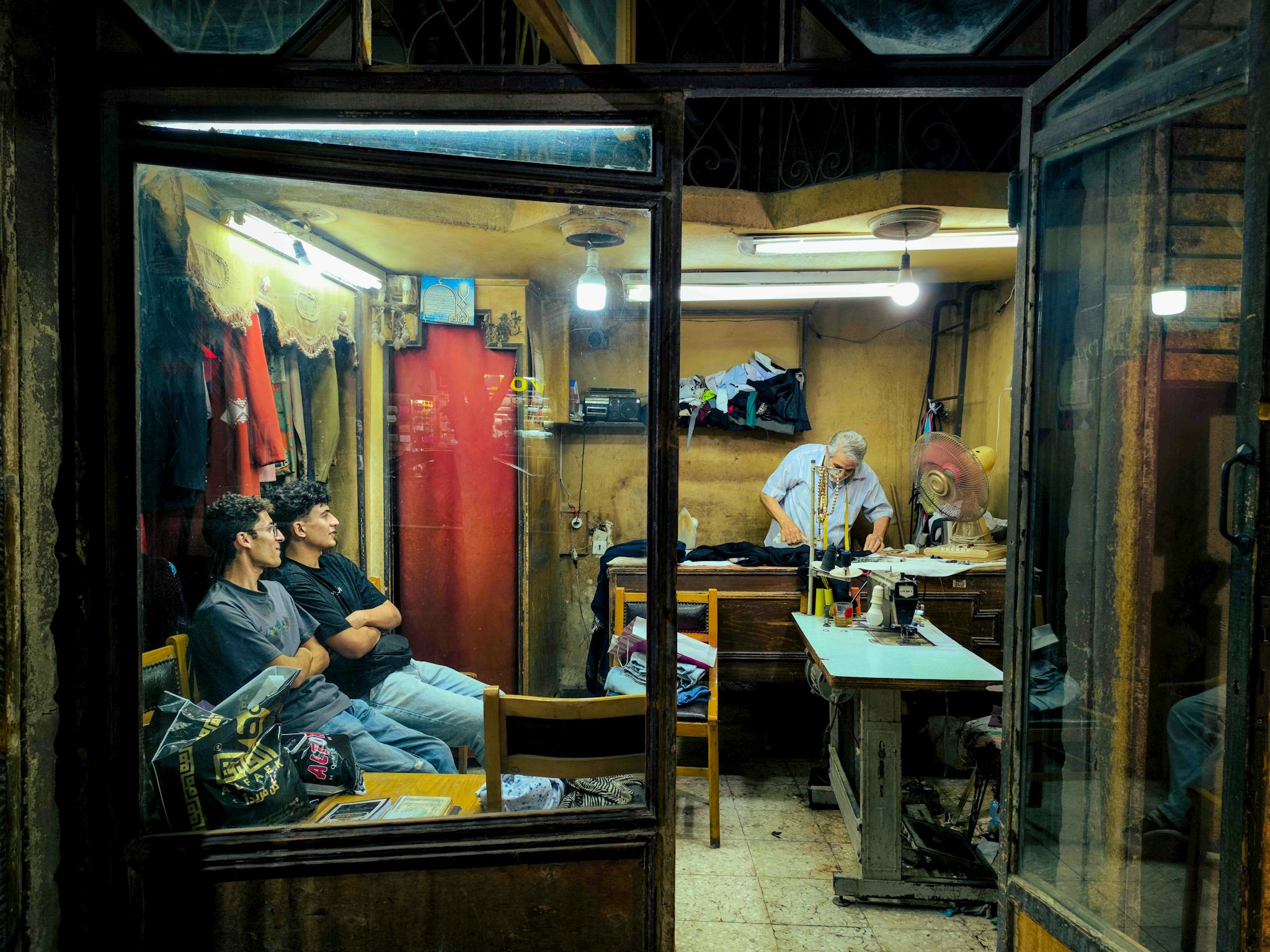Intimate view of a tailor shop with two men waiting and a tailor at work. Cozy atmosphere.